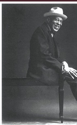 Tuts Washington seated at the piano, wearing a white hat